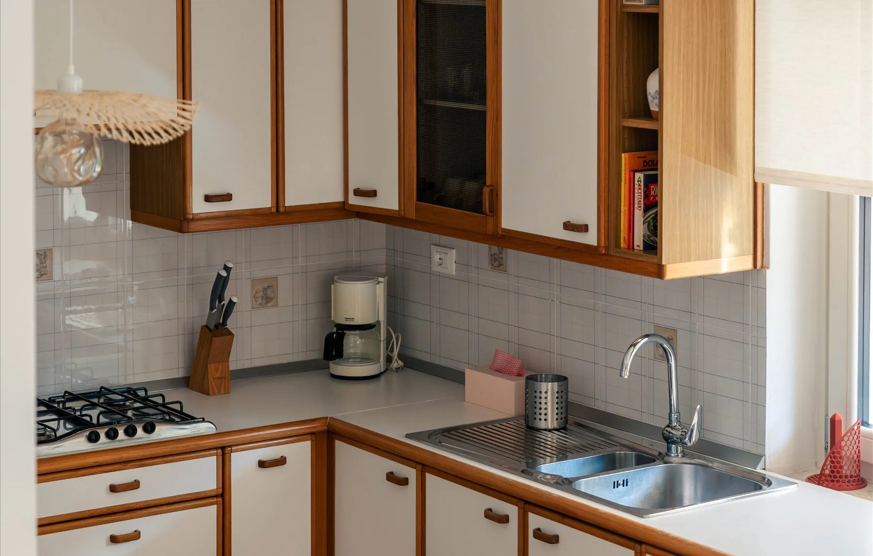 La cucina con mobili bianchi e legno, piano cottura a gas e lampada in rattan