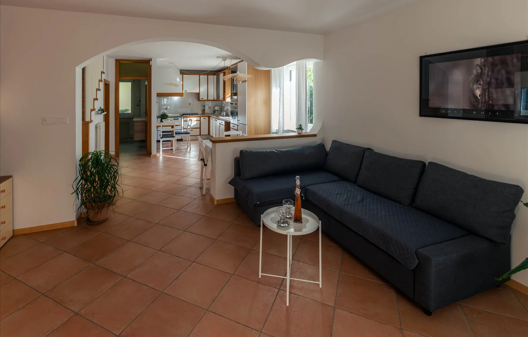 Il soggiorno open space con divano angolare, piante e l'arco che apre sulla cucina